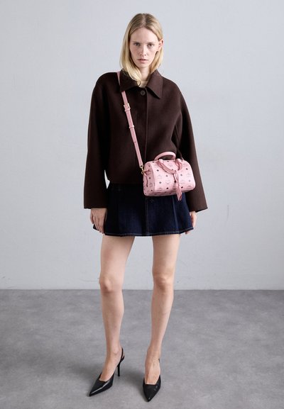 Cămașă din lână de culoare maro, fustă mini din denim, tocuri negre cu vârf ascuțit și o geantă roz cu model, care are mânere superioare și curea pentru umăr.