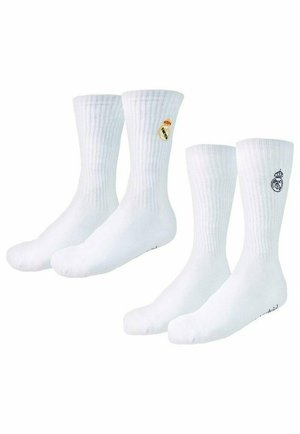 Cztery białe skarpetki typu crew z żebrowaną fakturą, dwie z nich z logo klubu piłkarskiego Real Madryt w różnych kolorach na okolicy kostki.