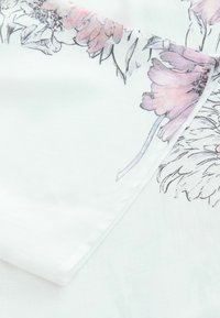 White fabric with floral patterns in pink and grey. Smooth texture with a slight sheen. Folded, revealing a soft drape and delicate design.
