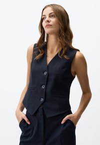 Marineblaue ärmellose Weste mit taillierter Passform, V-Ausschnitt, drei Knöpfen und zwei seitlichen Taschen für zusätzliche Funktionalität.