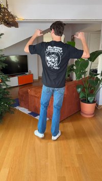 Sort t-shirt med et grafisk motiv af en ulv og tekst. Kombineret med lyseblå jeans og hvide sneakers i en hyggelig indendørs atmosfære.