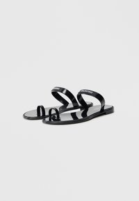 Black PVC sandals with two transparent straps and a toe ring. Smooth finish, minimalistic design, flat sole. Logo detail on straps.