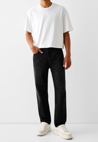 Camiseta de algodón blanca, corte relajado, combinada con jeans negros de pierna recta. Zapatillas blancas completan el atuendo, con un diseño de suela gruesa.