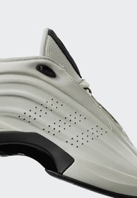 Krupan plan bijele tenisice sa strane koja prikazuje perforirani dizajn, podstavljen ovratnik i crnu potporu luka na potplatu.