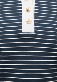 Ύφασμα με navy μπλε και λευκές ρίγες και λευκή λωρίδα με τρία χρυσά διακοσμητικά κουμπιά σε κάθετη σειρά.