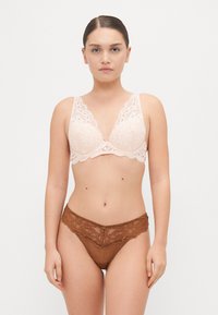 Krajková podprsenka v jemné růžové barvě s vlnitými okraji a středovou mašlí, spárovaná s hnědými krajkovými kalhotkami s průsvitnou tkaninou a květinovými vzory.
