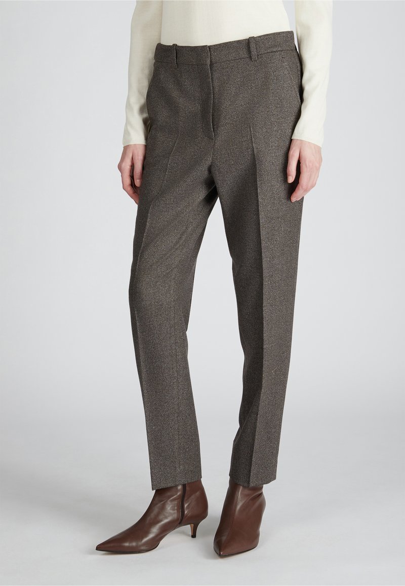 Bruine gestructureerde broek met een getailleerde pasvorm, voorzien van plooien en een tailleband. Gecombineerd met bruine spitse enkellaarsjes.