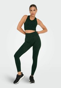 Set di abbigliamento attivo di colore verde scuro, composto da un top corto e leggings a vita alta, entrambi con una sottile texture a stampa animale.