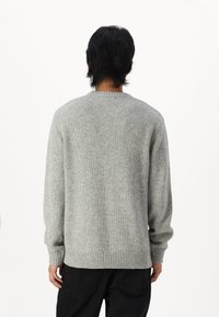 Pelēka adīta džemperis ar apaļu kakla izgriezumu, ribotu piedurkņu un apakšmalu, demonstrējot gludu tekstūru un brīvu piegriezumu. Attēlots aizmugurējais skats.