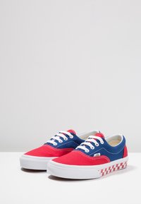 Rode en blauwe canvas sneakers met witte veters, voorzien van een geruite rood-wit patroon op de zool. Klassiek low-top ontwerp.