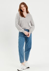 Grå, strikket sweater med V-hals og lange ærmer, parret med højtkort blå jeans og hvide sneakers. Enkel design med en afslappet pasform.