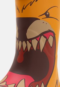 Botte en caoutchouc jaune avec un graphisme de monstre ludique, présentant des dents acérées et une bouche rugissante, accentuée par des détails marron et rose.