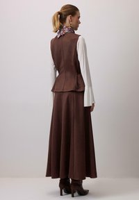 Rjavi antilop brezrokavnik z naborkom v pasu, združen z dolgo krilo. V območju ovratnika je viden vzorčast šal. Noge z gležnarji.