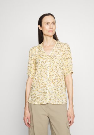 Απαλή κίτρινη μπλούζα με σχέδιο, με V-λαιμόκοψη, κοντά φουσκωτά μανίκια και κουμπιά μπροστά. Το ύφασμα φαίνεται μαλακό με μία ελαφριά γυαλάδα.