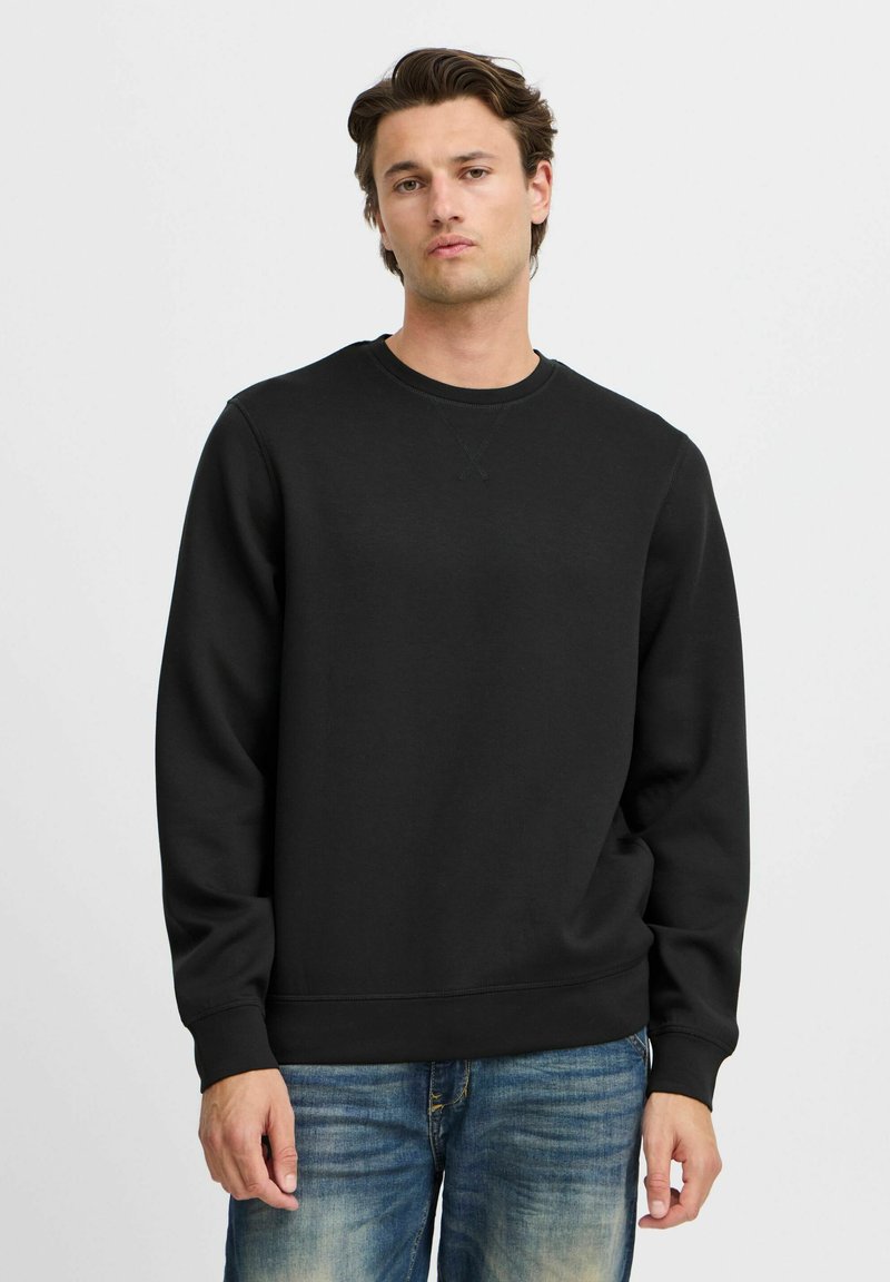 Zwarte katoen sweatshirt met een ronde hals, ribgebreide mouw- en zoomranden, en een gladde textuur, gedragen over lichtblauwe denim jeans.