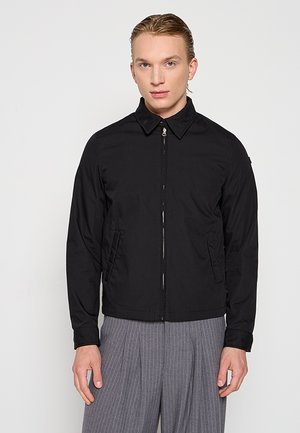Giacca nera con collo a camicia, chiusura frontale con zip e tasche laterali. Presenta una texture liscia e un design aderente.
