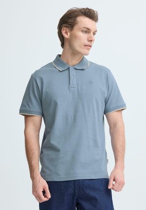 Hellblaues Poloshirt mit kurzen Ärmeln, kontrastierenden beigen Kragen und Bündchen sowie einem kleinen, auf der linken Brustseite gestickten Logo.