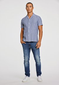 Lichtblauwe linnen shirt met korte mouwen, een notch-kraag en witte knopen, gecombineerd met donkerblauwe jeans en witte sneakers.