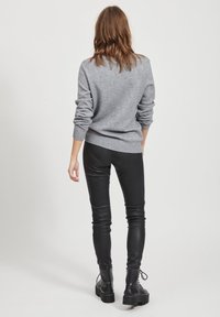 Pull gris en maille avec ourlet côtelé, associé à des leggings en cuir noirs et des bottes à lacets noires, vu de dos.