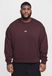Sudadera Nike cor de bordô com decote redondo e mangas compridas, com um pequeno logótipo branco no peito. Tecido macio e corte descontraído.