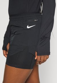 Nike mustat urheilushortsit, joissa on tiukka muotoilu, jossa on vetoketjullinen tasku ja kontrastivärinen valkoinen logo. Valmistettu sileästä ja joustavasta kankaasta.