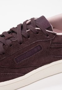 Mörklila mockasneaker med texturerad yta, prydd med snörning, gummisula och vadderad krage med en subtil logotyp.