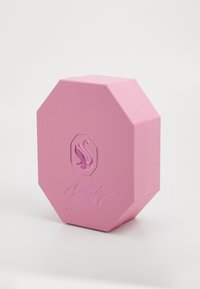 Rosa oktagonal boks med hevet svan logo og preget tekst "Ariana Grande." Lett tekstur med matt finish. Minimalistisk design.