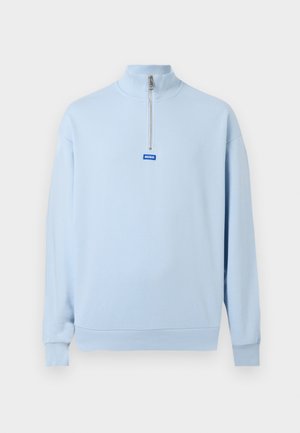 Pull-over à manches longues bleu clair avec un col montant et une fermeture éclair à moitié sur le devant, arborant un petit logo bleu "HUGO" en dessous de la fermeture éclair.
