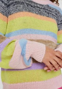 Margų mezginio megztinis su horizontaliomis juostelėmis: žalia, rožinė, mėlyna, levandų ir pilka. Yra raštuoti rankogaliai ir laisvas siluetas.