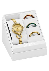 Ρολόι σε χρυσό τόνο με στεφάνι διακοσμημένο με κρύσταλλα, υφή στο χρυσό καντράν και λογότυπο "G". Περιλαμβάνει τρεις έγχρωμες διακοσμήσεις για το βραχιόλι μέσα σε κουτί.