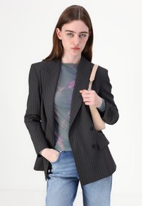 Blazer à fines rayures sombres superposé à un haut floral transparent. Associé à un jean bleu clair et un sac à main beige clair avec une anse.