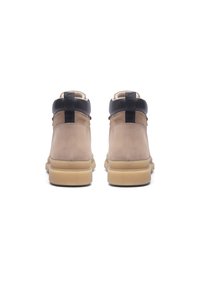 Tan mockasins av mocka med svarta läderdetaljer, som har en bred sula och en minimalistisk design, med slät textur och robust konstruktion.