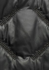 Czarna pikowana tkanina z wzorem w kratkę, z wytłoczonym logo "lululemon" na krawędziach, prezentująca gładką, refleksyjną fakturę.