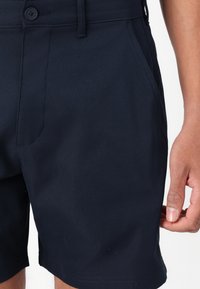 Marineblå shorts laget av lett stoff, med knappestenging, sidelommer, og en jevn tekstur. Kort lengde design.