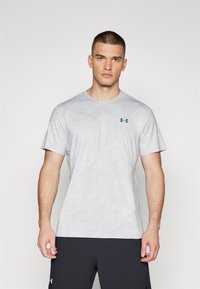 Camiseta deportiva gris claro con un patrón texturizado, cuello redondo, mangas cortas y un pequeño logo azul y verde en el lado izquierdo del pecho.