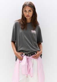 T-shirt en coton gris à manches courtes, arborant le texte "MOCHITO MORNINGS" en rose. Associé à un pantalon blanc et un foulard rayé rose.