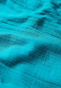 Turquoise stof met een zachte, gestructureerde oppervlakte, met subtiele kreukels en kleurvariaties die de lichte kwaliteit benadrukken.