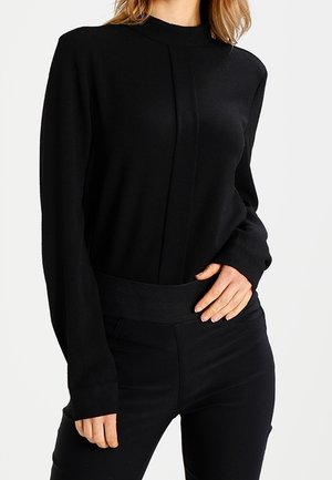 Maglia nera a maniche lunghe con collo alto, design strutturato e cintura arricciata. Texture liscia con un'estetica minimalista.