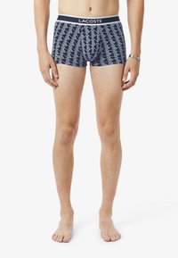 Boxers navy con un patrón geométrico blanco, cintura elástica con el logo "LACOSTE" y un diseño ajustado. Material suave de algodón.