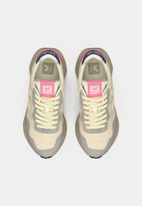 Μπεζ αθλητικά παπούτσια με επάνω μέρος από δίχτυ, γκρι λεπτομέρειες, ροζ ετικέτες στη φτέρνα και λευκά κορδόνια. Στρογγυλεμένη μύτη και υφασμένα πέλματα για καλύτερη πρόσφυση.