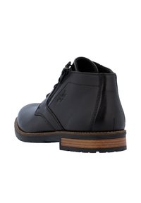 Botín negro de cuero hasta el tobillo con punta redonda, cremallera lateral y acentos de costura. Presenta un tacón marrón con aspecto de madera rayada.