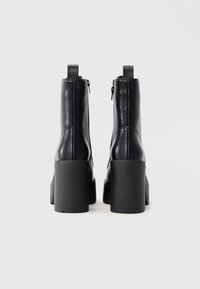 Μαύρες δερμάτινες μπότες μέχρι τον αστράγαλο με χοντρές πλατφόρμες, με απαλή υφή, πλαϊνούς φερμουάρ και κομψό σχέδιο.