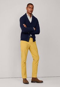 Navy ribbed shawl collar cardigan over a light shirt, paired with yellow trousers and brown ankle boots. The outfit combines various textures.