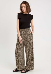 Haut sans manches noir associé à un pantalon large taille haute en imprimé léopard. Texture lisse avec une taille élastique pour le confort.