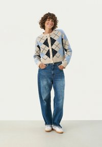 Sweter kardigan w jasnym beżu, niebieskim i granatowym z wzorem argyle, z okrągłym dekoltem i białymi guzikami; w połączeniu z luźnymi dżinsami.