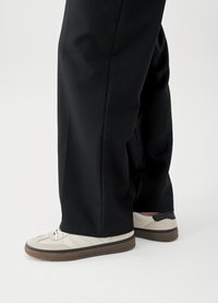 Baskets blanches avec des accents gris clair, semelles en caoutchouc et lacets plats, associées à un pantalon noir ample. Design simple et style décontracté.