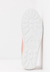 Gros plan sur une semelle de chaussure en caoutchouc blanc avec un motif de prise texturé et le nom de la marque "Blackstone" incrusté, la chaussure repose debout contre un mur.