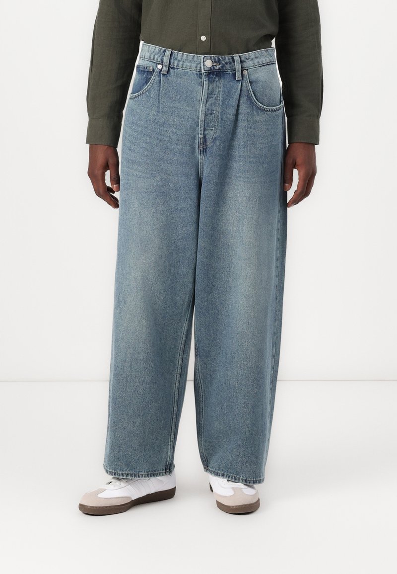 Ljusblå, vida denimjeans med fem fickor, bältesöljer och subtil blekning. Tillsammans med vita och beige sneakers.