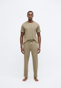 Σετ χαλαρής ένδυσης σε χακί, που αποτελείται από κοντομάνικο πουκάμισο με ριγωτή υφή και παντελόνι με κορδόνι, κατασκευασμένα από μαλακό ύφασμα.