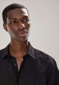 Camicia nera con un delicato motivo floreale, realizzata in tessuto liscio, con colletto classico e chiusura frontale con bottoni.